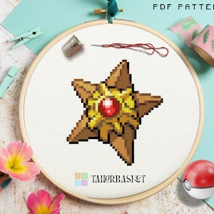 May include: A cross-stitch pattern of a pixelated starfish with a red gem center, set in a wooden embroidery hoop. The design features shades of brown, gold, and red. The text "PDF PATTERN" is at the top, and the TailorBasket logo is at the bottom.