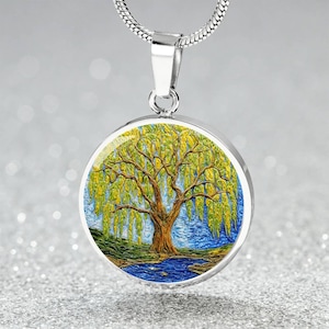 May include: A silver-toned pendant necklace featuring a round charm with a colorful painting of a willow tree. The tree has a brown trunk, green and yellow leaves, and is set against a blue sky and water.