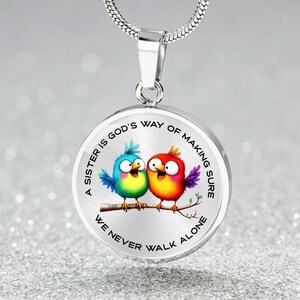 May include: A silver necklace with a round pendant featuring two cartoon birds and the text "A sister is God's way of making sure we never walk alone".
