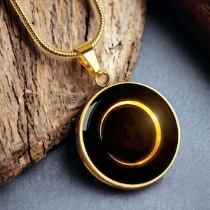 Puede incluir: Collar dorado con un colgante circular. El colgante presenta un centro negro con un diseño de media luna dorada brillante. La cadena y el marco del colgante también son dorados. El colgante mide aproximadamente 3,8 cm de diámetro.