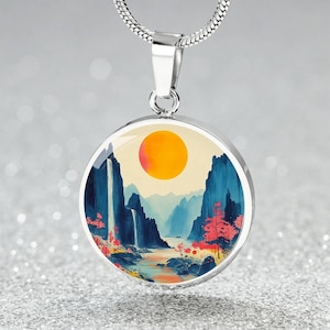 May include: A silver necklace with a round pendant featuring a watercolor painting of a mountain landscape with a waterfall, a river, and a bright orange sun.