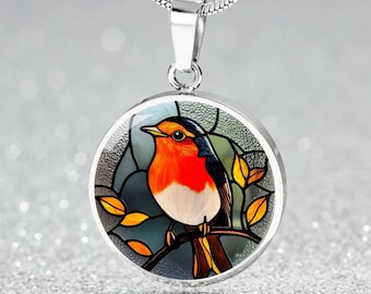 May include: A silver necklace with a round pendant featuring a stained glass style robin perched on a branch with yellow leaves. The robin has a red breast, white belly, and black wings.