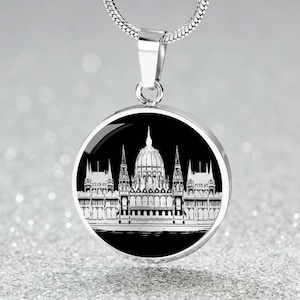 May include: Silver-toned necklace featuring a round pendant with a black background. The pendant displays a white architectural illustration of a building with a central dome and multiple spires. The chain is a thin, silver snake chain.