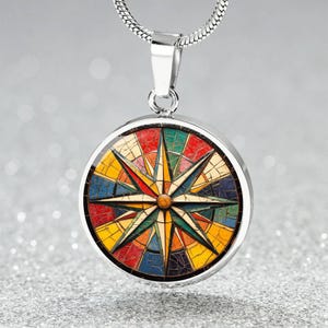 May include: A silver-toned pendant necklace featuring a round pendant with a colorful compass rose design. The compass rose has a starburst pattern in shades of red, yellow, blue, and green. The pendant hangs from a silver chain.