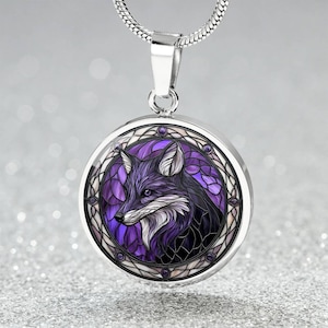 May include: A circular silver pendant featuring a purple and black fox design. The pendant is suspended from a silver chain. The fox illustration has a stained glass effect, with a white and purple background.