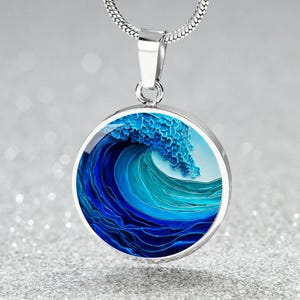 May include: A circular silver pendant necklace featuring a vibrant ocean wave design in shades of deep blue, turquoise, and white. The pendant hangs from a silver snake chain, showcasing a detailed, swirling water graphic within a polished frame.