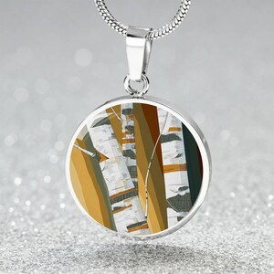 May include: A silver-toned pendant necklace featuring a round pendant with an abstract design of birch trees in shades of brown, white, and yellow. The pendant hangs from a delicate silver chain, creating a nature-inspired accessory.