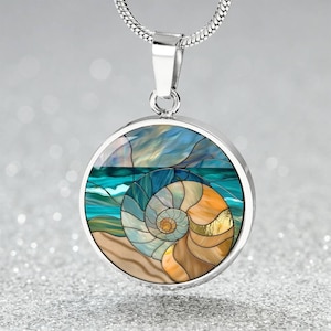 May include: A silver-toned pendant necklace with a round, stained-glass style design. The pendant features a spiral seashell design with ocean and beach elements in shades of blue, teal, orange, and tan. The necklace has a silver chain.
