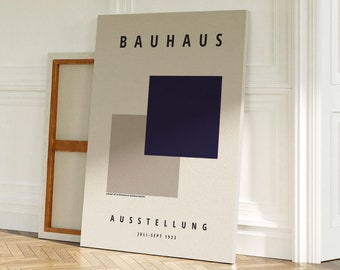 Puede incluir: Un póster beige con el texto "BAUHAUS AUSSTELLUNG 1923-1933" y un diseño geométrico de un cuadrado azul oscuro superpuesto a un cuadrado marrón claro. El póster está apoyado contra una pared blanca con zócalos.