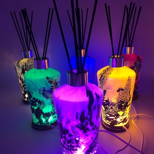 Könnte beinhalten: Fünf Glasdiffusor-Flaschen mit schwarzen Schilfrohren und bunten Lichtern. Die Flaschen sind mit schwarzer und weißer Marmorierung verziert und haben verschiedene Farben, darunter Grün, Blau, Gelb und Lila.