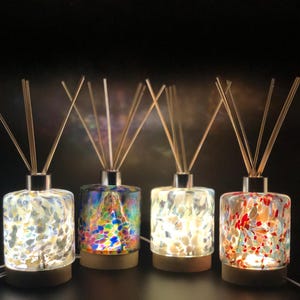 Può includere: Quattro bottiglie diffusore in vetro con basi in legno e bastoncini. Le bottiglie sono riempite con vetro colorato e macchiato. Le bottiglie sono illuminate dall'interno, creando un bagliore caldo.