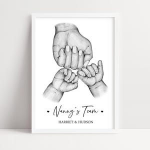 May include: A framed black and white pencil sketch print featuring one large hand holding two smaller hands. Below the illustration, the text reads Nanny's Team with a heart on each side, followed by the names HARRIET & HUDSON in capital letters.