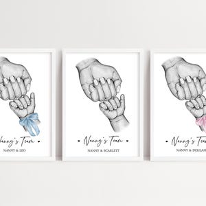 May include: Three framed prints featuring a black and white pencil sketch of an adult hand holding a baby hand. Each print includes the text Nanny's Team and a name, with one baby hand wearing a blue ribbon and another wearing a pink ribbon.