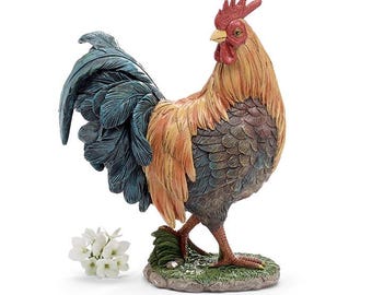 May include: A detailed figurine of a rooster, featuring a red comb and wattle, with a mix of orange, brown, and blue feathers. The rooster stands on a small, grassy base, with a few white flowers nearby. The sculpture is a decorative item.