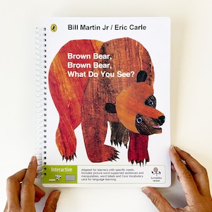 May include: A brown bear with blue eyes and a red scarf is featured on the cover of a book titled "Brown Bear, Brown Bear, What Do You See?" by Bill Martin Jr. and Eric Carle. The book is part of the Interactive series, adapted for learners with specific needs.