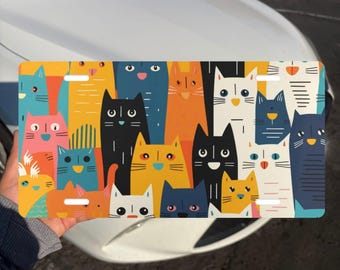 Puede incluir: Una placa de matrícula rectangular con un patrón colorido y repetitivo de gatos estilizados en varios tonos de azul, naranja, amarillo, rosa, negro y blanco. Los gatos tienen rasgos faciales simples y están dispuestos en un diseño denso.