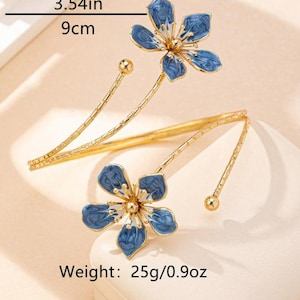May include: Gold-coloured arm cuff with two blue flower designs. Each flower has five petals with a blue enamel finish. The cuff is 9 cm long and weighs 25g.