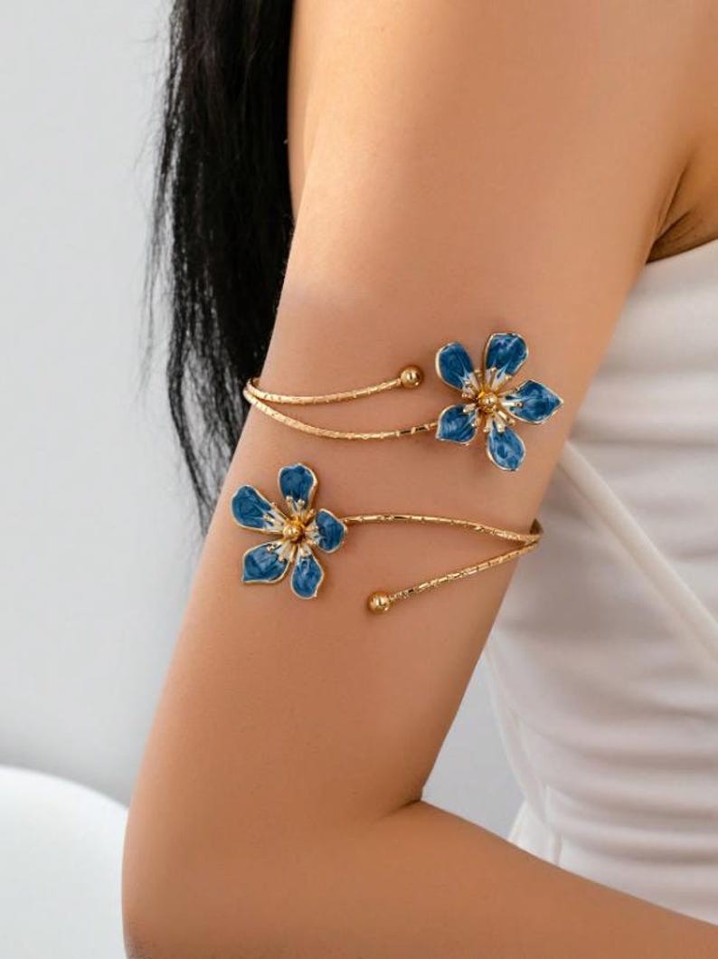 May include: Gold arm cuff with two blue flower designs and gold centres. The floral accents are linked by delicate gold bands, creating an elegant accessory. This arm cuff is a stylish piece of jewellery, perfect for adding a touch of glamour.