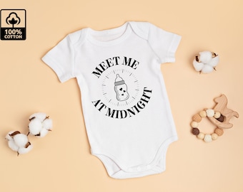 May include: White baby onesie with the text "MEET ME AT MIDNIGHT" in black. The design includes a baby bottle illustration. The onesie is surrounded by cotton buds and a wooden toy on a beige background. 100% cotton.