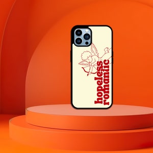 Puede incluir: Una funda blanca para iPhone con un gr&aacute;fico rojo y blanco de un cupido con una flecha y el texto "hopeless romantic".