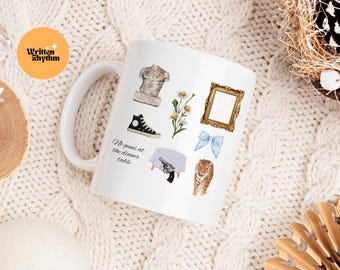 May include: White ceramic mug decorated with various watercolor illustrations, including a bust, a high-top sneaker, a gold frame, a blue bow, a tiger, and a table with a gun. The mug also features the text "No guns at the dinner table."