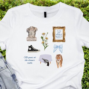 May include: White t-shirt with a variety of graphics, including a statue, a pair of sneakers, a bouquet of daisies, a bow, a table setting, a gun, a tiger, and a framed quote that reads "It's the great undoing of my heart as I know it".