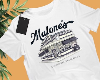 May include: A white t-shirt featuring a dark blue graphic of a retro diner building with the text "Malone's" above it and "BEST BURGERS IN HASTINGS, MA" below it. A black rectangular tag is attached to the collar with a thin black string.
