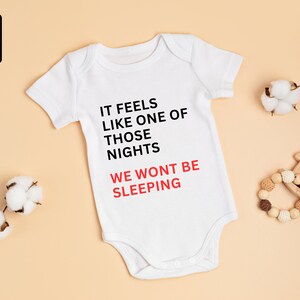 Könnte beinhalten: Weißer Baby-Strampler mit kurzen Ärmeln und dem Text "It feels like one of those nights we won't be sleeping" in Schwarz und Rot.