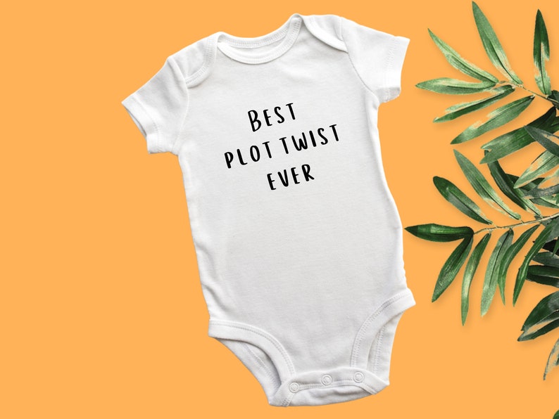 May include: White baby onesie with black text that reads "Best Plot Twist Ever".
