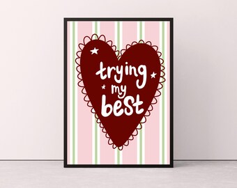 May include: A framed art print featuring a burgundy heart with a scalloped edge and the words "trying my best" in white script. The background has pink and green vertical stripes.