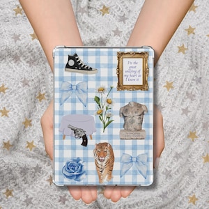 May include: A tablet case with a blue and white gingham pattern, decorated with various illustrations. These include a black high-top trainer, a bow, a table with a gun, a tiger, a rose, and a framed quote.