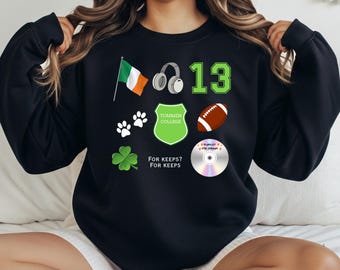 May include: Black sweatshirt with green and white graphics. Features an Irish flag, headphones, the number 13, paw prints, a shamrock, a football, a CD with text, and a Tommen College crest. Text on the sweatshirt reads "FOR KEEPS? FOR KEEPS".