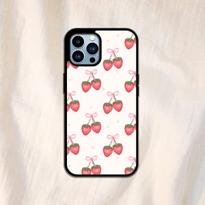 K&ouml;nnte beinhalten: Eine schwarze Handyh&uuml;lle mit wei&szlig;em Hintergrund und einem sich wiederholenden Muster aus roten Erdbeeren mit rosa Schleifen.