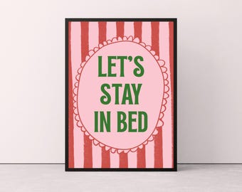 May include: A framed print with the text "LET'S STAY IN BED" in green letters on a pink oval, set against a pink and red striped background. The frame is black.