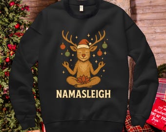 May include: Black sweatshirt with a cartoon reindeer wearing a Santa hat, meditating in a lotus position. The reindeer is surrounded by Christmas ornaments and stars. The text "NAMASLEIGH" is printed below the reindeer.