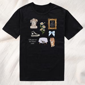 May include: Black t-shirt with a white graphic design featuring a statue, flowers, a shoe, a table, a gun, a bow, and a tiger. The text on the shirt reads "I'm the great undoing of my heart if I knew it" and "No guns at the dinner table."