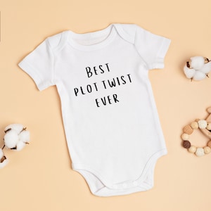 May include: White baby onesie with short sleeves and the text "Best Plot Twist Ever" printed in black.