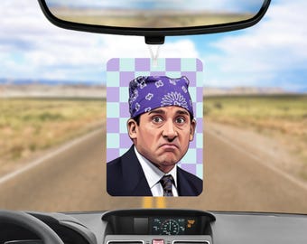 May include: A rectangular car air freshener featuring a cartoon illustration of a man wearing a purple bandana with white floral patterns. The man has a somber expression, wears a dark suit with a white shirt and tie, set against a light purple and white checkered background.