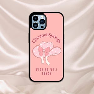 Puede incluir: Una funda de iPhone rosa con un sombrero de lunares blancos y rosas con un lazo rosa y el texto "Chestnut Springs Wishing Well Ranch".