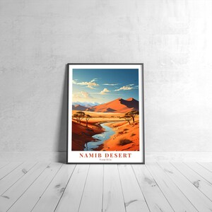 May include: A framed print depicting a desert landscape with a river flowing through it. The print features a red sand dune, a blue sky with clouds, and two trees. The text "NAMIB DESERT Namibia" is at the bottom of the print.