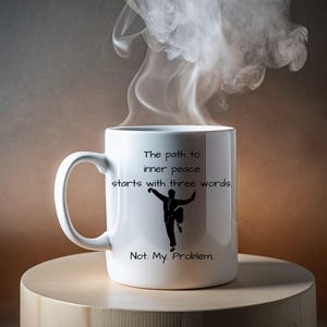 May include: White ceramic mug with a black silhouette of a person in a martial arts pose. The mug has the text "The path to inner peace starts with three words. Not. My. Problem."