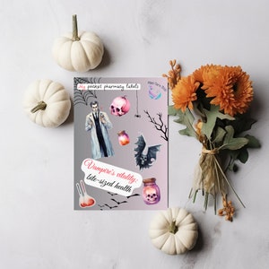 May include: A sticker sheet featuring illustrations of a vampire in a white coat, a pink skull, a bat, potion bottles, and test tubes. The text reads My pocket pharmacy labels and Vampire's vitality: bite-sized health, with spiderweb and bat motifs.