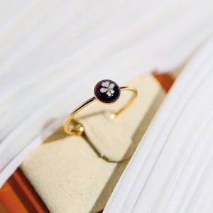 May include: A gold ring with a dark red round stone set in the centre. The stone has a white flower pressed inside.