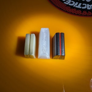 May include: Three small rectangular boxes, one gold, one white, and one black with a red stripe. The boxes are arranged in a row on a bright orange surface.