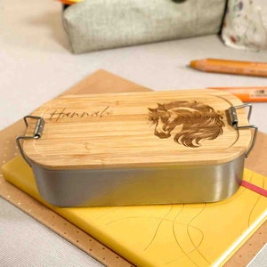 Könnte beinhalten: Eine rechteckige Bambus-Lunchbox mit einem Edelstahl-Innenraum. Der Deckel ist mit einem lasergravierten Pferdekopf-Design und dem Namen "Hannah" verziert.