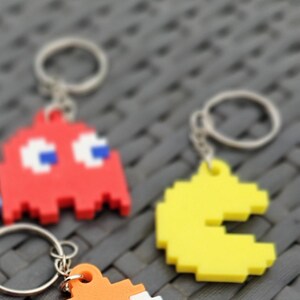 May include: Five colourful Pac-Man character keyrings with different coloured bodies and blue eyes. The keyrings are made of plastic and have a pixelated design.