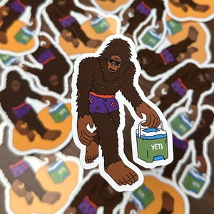 May include: A brown Bigfoot wearing purple and white patterned underwear and sunglasses is holding a green Yeti cooler with a blue lid. The cooler has the word "YETI" printed on it.