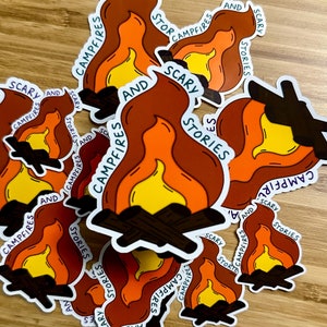May include: A collection of stickers featuring a campfire with flames and the text "Scary Stories and Campfires". The stickers are printed on white paper with a glossy finish.