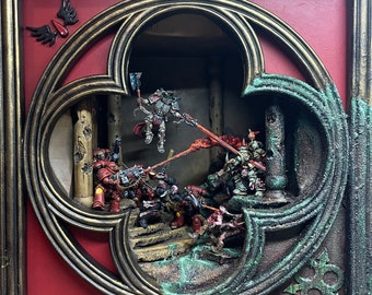 May include: A framed diorama featuring miniature figures in a battle scene. The frame has a gold finish with a gothic arch design. The figures are painted in various colors, including red, green, and silver, and are engaged in combat with energy blasts.
