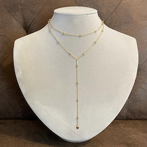 Peut inclure: Un collier en or à plusieurs rangs avec une longue chaîne pendante. Le collier est orné de petites perles rondes et d'un pendentif circulaire à l'extrémité de la longue chaîne.